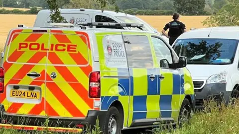 Three police vans parked on a field, with an officer looking away into the field.