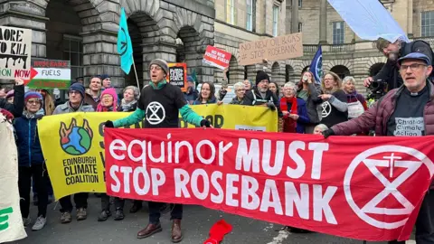 Dozens of campaigners standing outside the Court of Session holding large yellow and red banners calling for Equinor to stop Rosebank, and holding smaller signs and flags