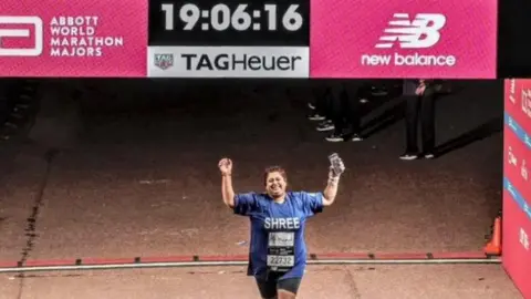 London Marathon Shreena crossing the finish line, wearing a blue top with her name on it