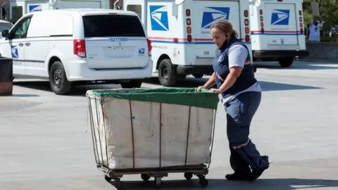 Reuters US Postal Service worker pushes a mail bin outside a post office in Royal Oak, Michigan (22 August 2020)