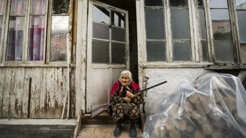 Getty Images Old woman stands in the entrance of her home with a rifle during the shelling of Stepanakert city