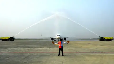 Getty Images A ground staff directs a Jazeera Airways aircraft to park as it receives a water canon salute upon landing at the newly built Gautam Buddha International Airport following its inauguration in Siddharthanagar on May 16, 2022.