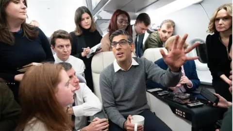 PA Media Rishi Sunak speaks to journalists on board a government plane to Dubai