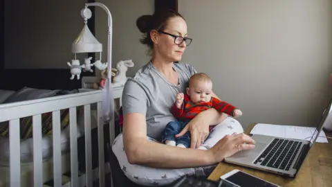 Getty Images Woman in front of a computer with a baby on her lap