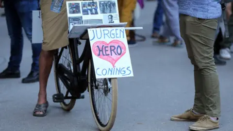 Getty Images A cyclist rides a bike with a banner in support to far-right Belgian soldier Jürgen Conings on 29 May