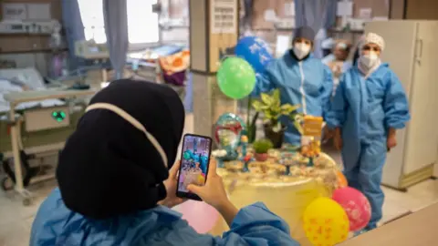 Getty Images Two Iranian medical personnel wearing protective suits pose for a photograph as they stand next to a Haft-Seen (Seven-S) table, The historical symbol for the Iranian New Year, in a COVID-19 ward in Firoozabadi hospital in Shahr-e-Rey neighborhood in the south of Tehran on the day of Nowruz
