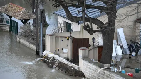 AFP A photo taken on 29 January 2018 shows a barrier erected in front of a house to block floodwater from the Seine river (L) in Bougival, west of Paris