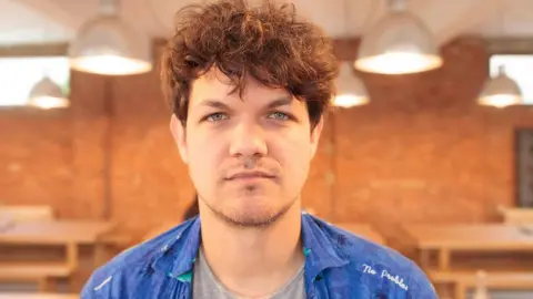 Gary Dooton Dan Gray looks straight into the camera wearing a blue jacket in front of a brick wall