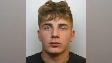 Mugshot of Kasper Stankiewicz who was convicted of Alfie Gray's death. He has short dark blonde hair and blue eyes. He is pictured against a plain, light background, looking straight at the camera with a blank expression.