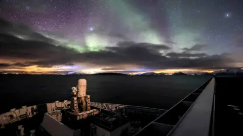 Crown copyright HMS Albion's bow against the backdrop of the Norwegian Fjords under the backlight of the Aurora Borealis