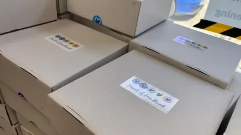 Brown boxes in a pile. They have Heart of Headland stickers on the lid.