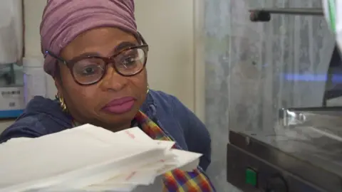 Endurance Obabueki standing behind the counter of her cafe in Harpurhey