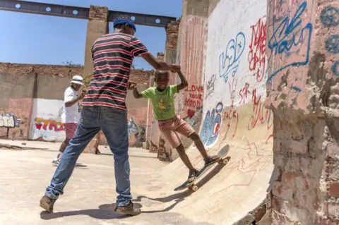 Getty Images A man holds a child's hands as he skateboards down a ramp.