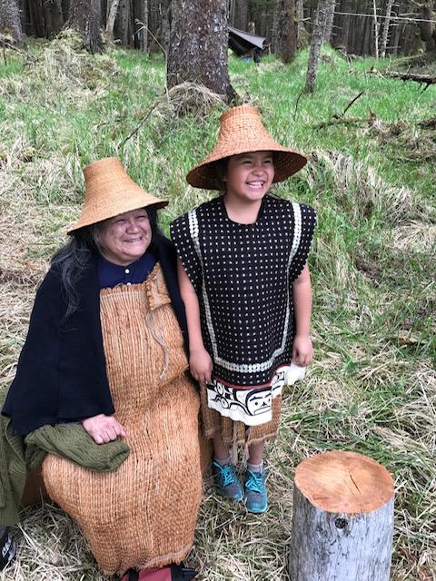 Diane Brown in traditional Haida hat and woven shawl with her granddaughter in the woods