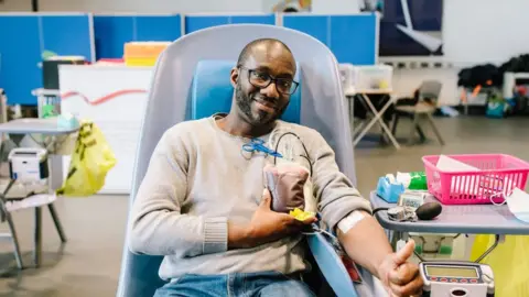 NHS Blood and Transplant Black man giving a thumbs up while he donates blood