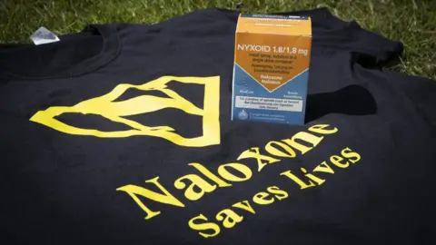 Mandy Jones T shirt with Naloxone saves lives and box of naloxone