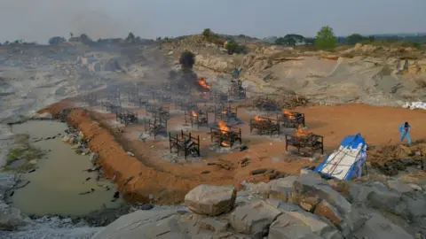 Getty Images Burning pyres of the victims who died of Covid-19 coronavirus are pictured at an open air crematorium set up for the coronavirus victims inside a defunct granite quarry on the outskirts of Bangalore on May 1, 2021