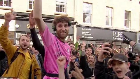 Dom Whiting on a bike surrounded by cheering people
