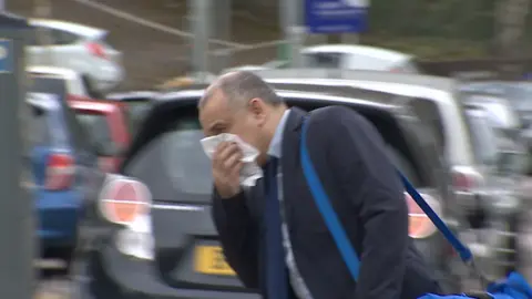 BBC Rajesh Lama arriving at Newport Crown Court - he is trying to hide his face with a tissue. He is wearing a suit and had a blue holdall bag over his shoulder
