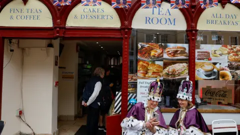 Reuters Royal fans dressed in royal-themed costumes sit outside a bar while waiting for the Coronation concert at Windsor Castle