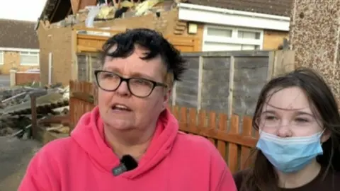 Marie Richards and her daughter Amy outside their home, which is surrounded by rubble