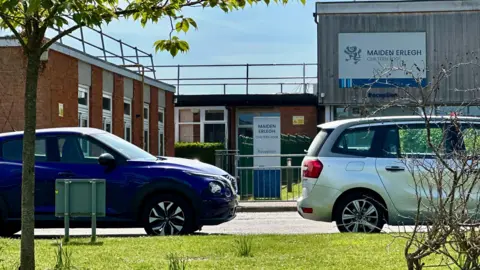 The exterior of Maiden Erlegh Chiltern Edge school pictured in the sunshine with two car parked outside.