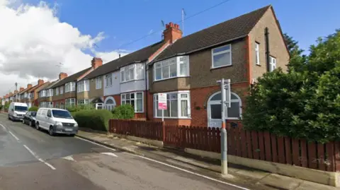 A Google Streetview image of a property on a residential road. It is an end-of-terrace house with on-street parking.