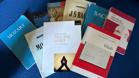 Martin Heath/BBC A selection of choral and orchestral sheet music books spread across a blue surface, including scores by Mozart, Bach, Mendelssohn, Britten and John Rutter. Titles visible include Requiem, Elijah, Feel the Spirit, and Dream of Gerontius, with covers overlapping in a loose arrangement.