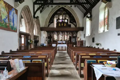 Church in Wales The inside of a church with wooden benches and stained glass windows.