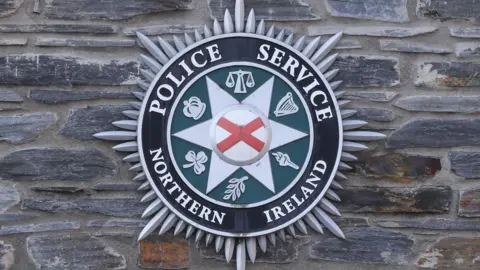 PA Images Police Service of Northern Ireland crest on a stone wall.