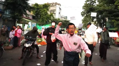 Tayzar San/Facebook Tayzar San distribuindo panfletos boicotando as eleições, junto com outras pessoas em uma rua movimentada.