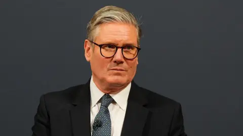 Getty Images UK Prime Minister Keir Starmer attends a press conference. He is wearing a dark navy suit, white shirt and a patterned tie.