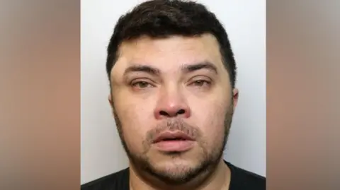 A custody image of Wesley Brito. He has short dark hair and dark stubble. There is a large lump above his right eye