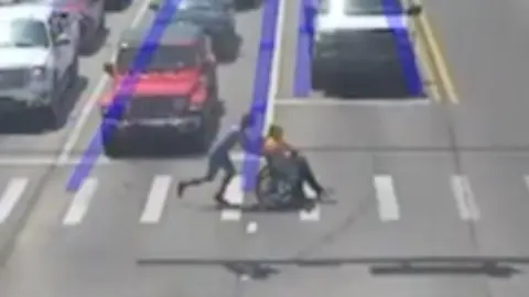 Man dressed as Spider-Man pushes wheelchair user across a crossing