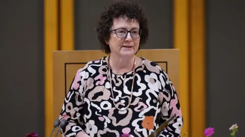 AP The image shows the Senedd's presiding officer Elin Jones speaking in the debating chamber. She is wearing a patterned top and glasses.
