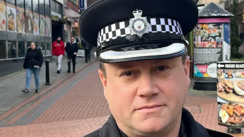 Superintendent Jon Bowcott in Wrexham city centre. He is wearing a police-issue hat and people can be seen walking along the street over his shoulder