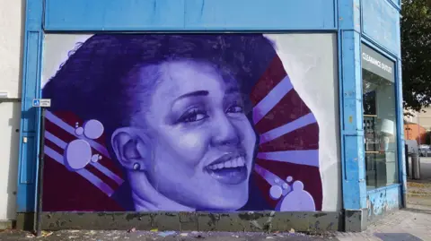 Jack Sankson A mural of singer Beverley Knight on the side of a shop. It is painted in purple and shows the singer smiling.