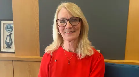 Shirley Congdon, wearing glasses and a red top, smiling.