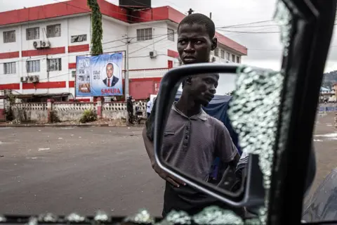 John Wessels/AFP Men try to fix a car that had its windows smashed and tyres slashed in Freetown, Sierra Leone