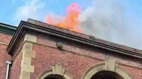 Sarad Yousaf Flames from the top of a red brick building