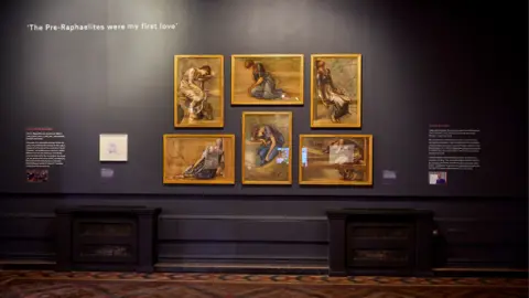 David Rowan/Birmingham Museums Trust Five portraits in yellow/gold frames are hung on a dark-coloured wall. On either side of them there is white writing on the wall, the writing is too small to read