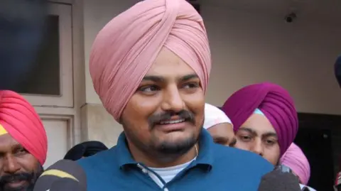 Getty Images Sidhu Moose Wala pictured in 2020. Sidhu is an Asian man with a pale pink turban, short moustache and a beard. He wears a blue polo shirt.