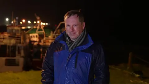 Chris Page, caught in a downpour, wearing a blue and black rain jacket with a striped scarf