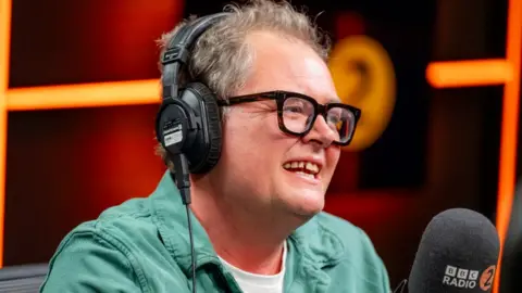 Alan Carr in the Radio 2 studio, wearing a green shirt