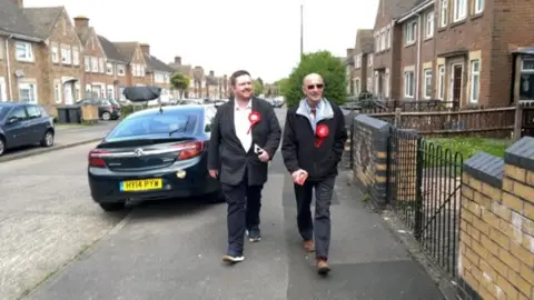 Terry Pullen and a fellow volunteer walking along a street with houses either side