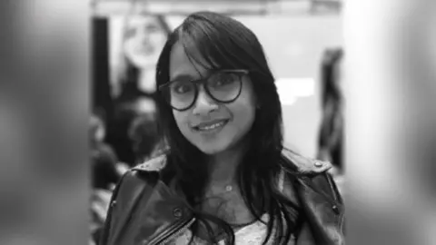 University of Cambridge Smiling woman with long dark hair and glasses.