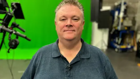 Sentireal CEO Tom Houston sits in front of a greenscreen