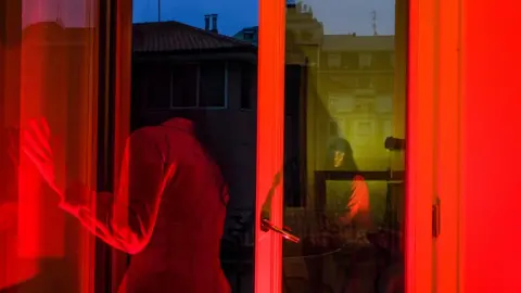 Lucia Buricelli A red-tinted photograph shows Lucia staring outside of her window