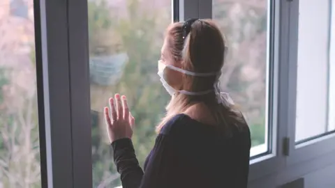 Getty Images woman in mask looking out window