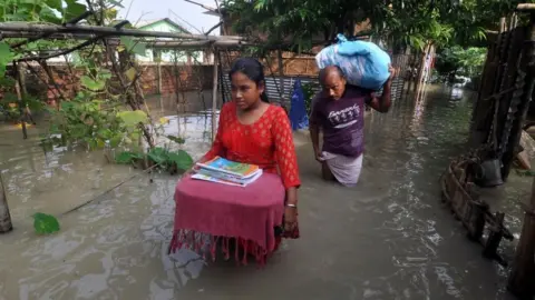 Getty Images Villagers move to a safer place from the flooded area of Hatisela in Kamrup district of Assam.